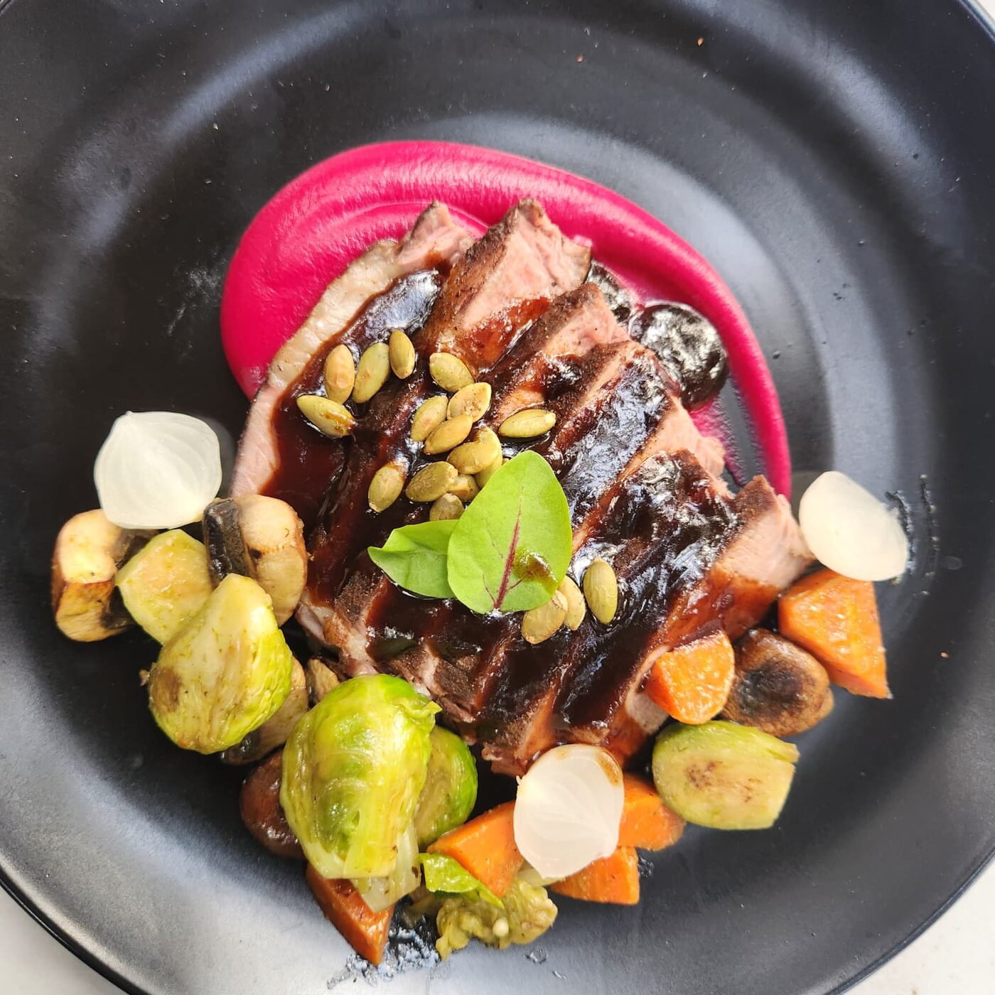 Sliced pork with beet purée, roasted vegetables, and pepitas